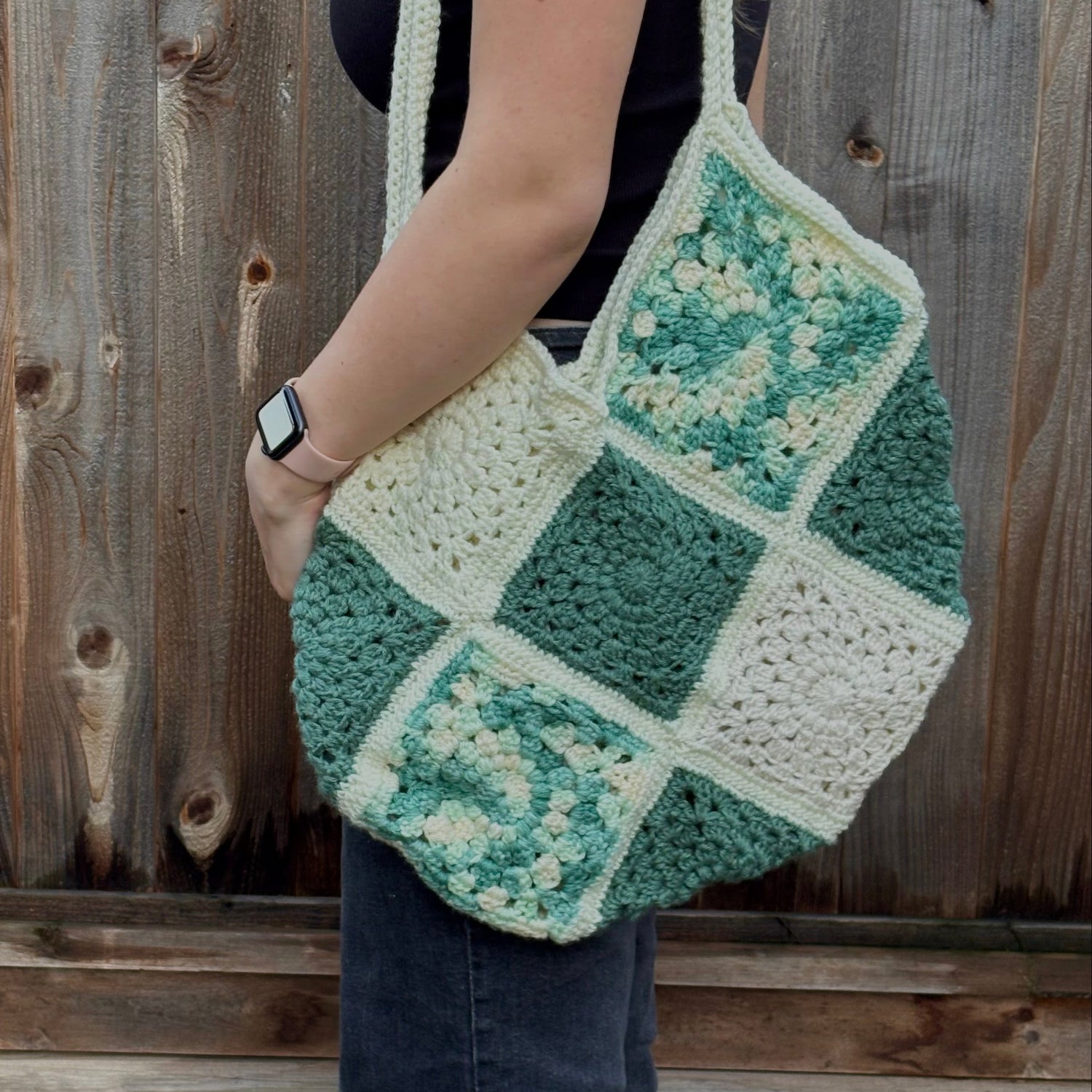 Person holding a green and white crocheted bag against a wooden background